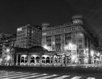 Illuminated buildings by road against sky in city at night