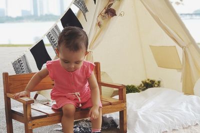 Cute baby girl looking down while sitting on chair by tent