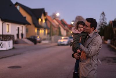 Father embracing and kissing sad daughter while standing outdoors during sunset