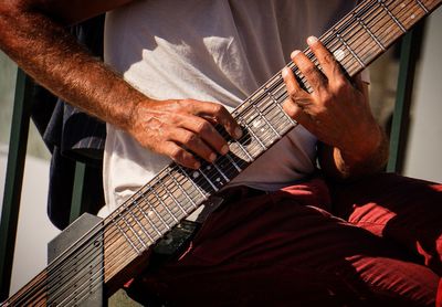 Midsection of man playing string instrument while sitting on chair