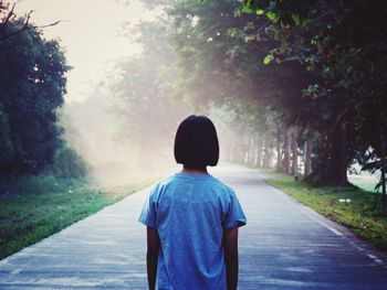 Rear view of man standing on road amidst trees