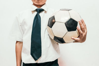 Midsection of boy with soccer ball standing against white background