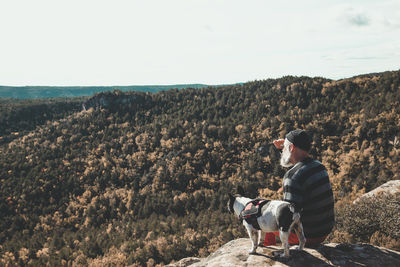 Man sitting with dog on cliff against mountain range