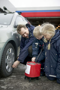 Man checking air pressure in tire with children