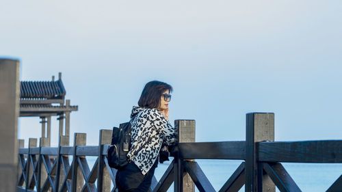 Woman standing by railing against clear sky