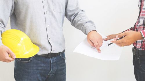 Midsection of architect pointing while colleague holding document over white background