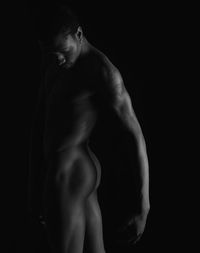 Naked man against black background