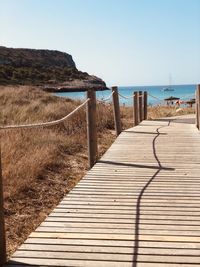 Boardwalk leading towards sea against clear sky