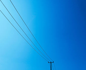 Low angle view of electricity pylon against clear blue sky