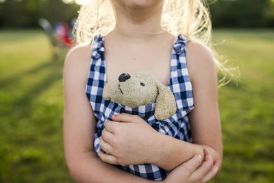 Midsection of girl holding stuffed toy in dress on field at backyard
