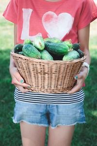 Midsection of woman holding basket full of cucumbers