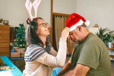 Middle-aged couple having fun while the woman puts the christmas hat on the man's head.