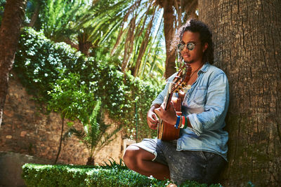 Young woman sitting on plant by tree