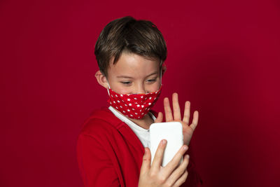 Boy wearing mask using mobile phone against red background