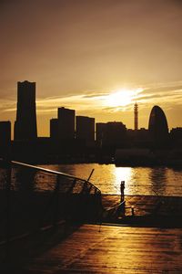 Silhouette buildings by river against sky during sunset at minato mirai 21