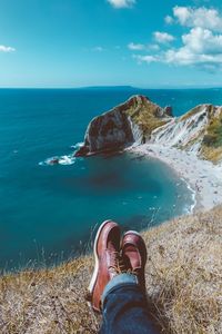 Low section of man sitting on cliff against sea