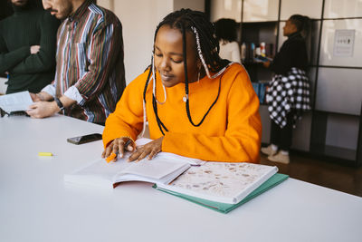 Young woman with braided hair studying while sitting at university