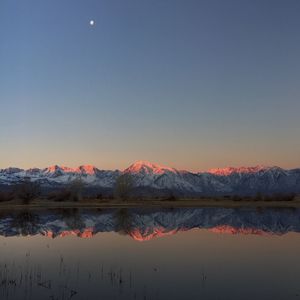 Idyllic shot of snowcapped mountains reflection in lake against clear sky during sunrise