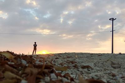 Rear view of man standing on sand against sky during sunset