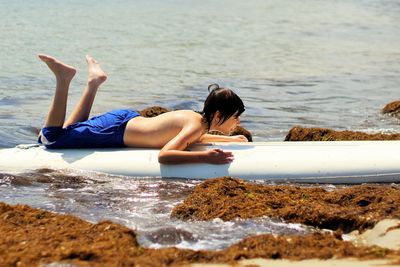 Full length of shirtless boy surfboarding at sea shore