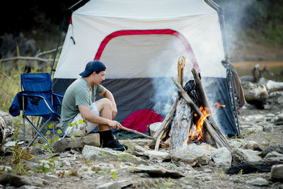 Side view of young man sitting at campsite during sunset