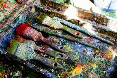 Close-up of messy paintbrushes in dirty colorful stained container on table