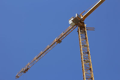 Low angle view of crane against clear blue sky