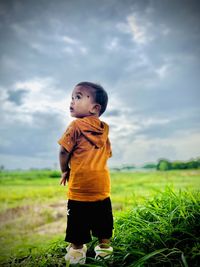 Side view of boy standing on field against sky