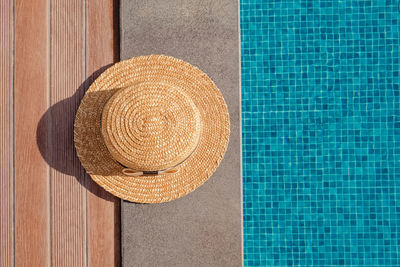 Woman's straw hat lying on the edge of the swimming pool with blue water, top view. 