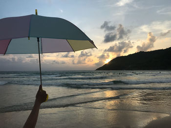 A girl holds a colorful umbrella on the beach with sunset near hill and sunlight reflects on the sea