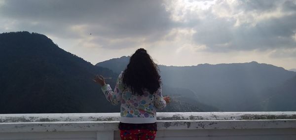 Rear view of woman standing by mountain against sky