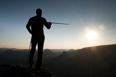 Tourist guide show the right way with pole in hand. hiker with sporty backpack on rock.