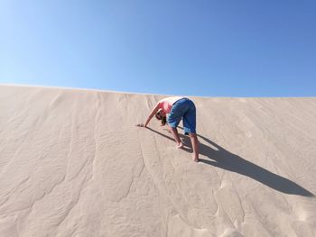 Low angle view of woman on sand dune against clear blue sky