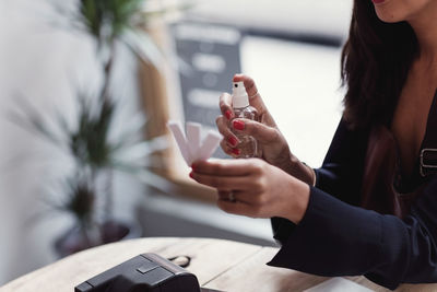 Midsection of woman spraying perfume on litmus strips at workshop