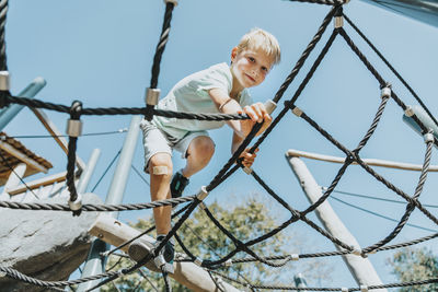 Boy climbing on spider web in public park during sunny day