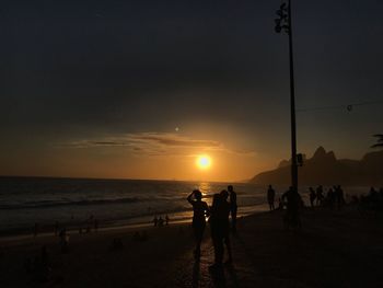 Silhouette people on beach against sky during sunset