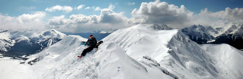 Person sitting on snow heap against sky