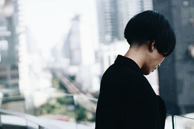 Side view of woman with short hair standing against buildings in city