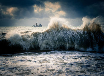 Panoramic view of waves splashing on sea against sky