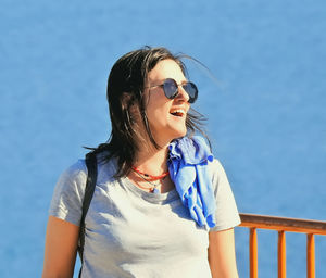Young woman looking away while standing against blue sky