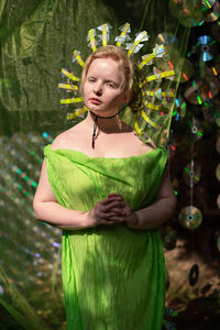 Young woman in mirrored mask and neon fabric standing in forest  front of the scenery from a cd case