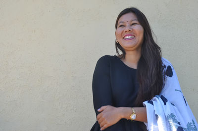 Portrait of a smiling young woman standing against wall