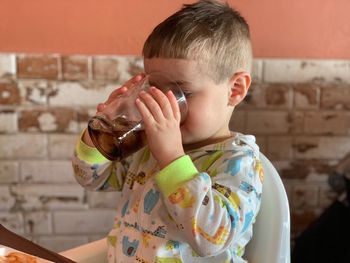 Close-up of boy drinking juice while sitting on high chair against wall