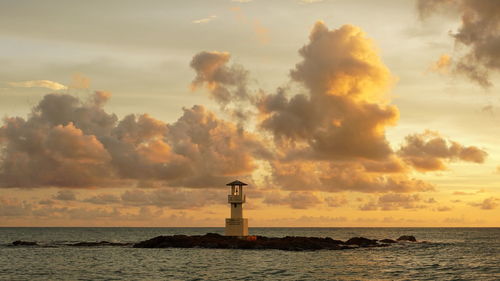 Lighthouse by sea against sky during sunset