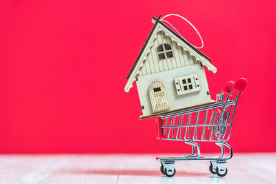Close-up of model home on small shopping cart against red background