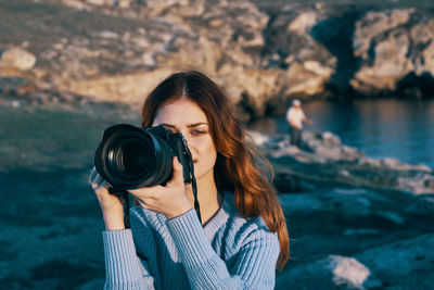 Portrait of woman photographing against sea