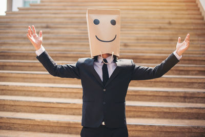 Businessman wearing smiling paper mask on steps in city