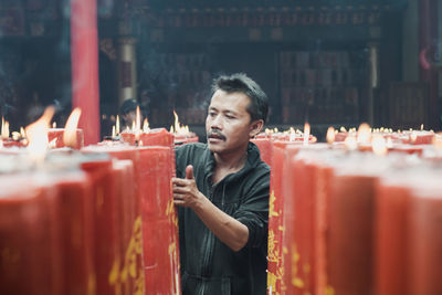 Mid adult man standing amidst lit candles in temple