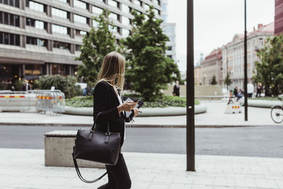 Side view of female entrepreneur with smart phone walking on sidewalk