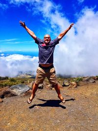 Full length of man with arms raised jumping against sky on sunny day